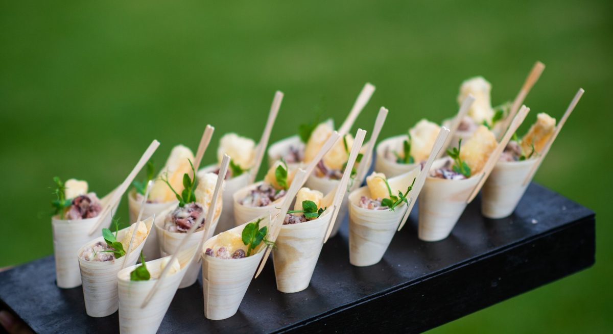 Fried Calamari Scampi Appetisers canapes being presented in bamboo cones and served at a party with selective focus.  It is being served at a wedding party.  A waiter is holding the tray with canapes.